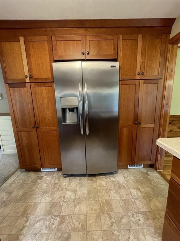 kitchen with stainless steel fridge, brown cabinets, and light countertops