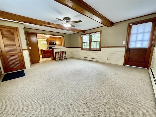 unfurnished living room with a wainscoted wall, beam ceiling, a ceiling fan, carpet floors, and baseboard heating