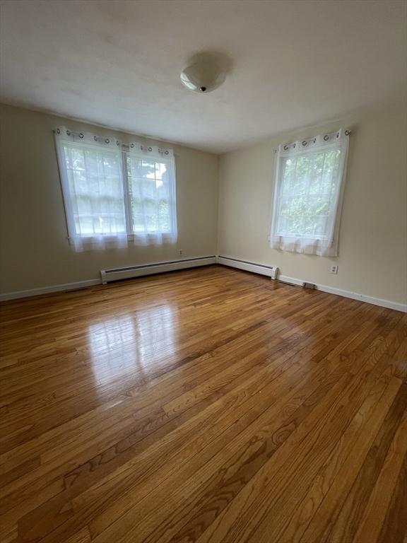 empty room with wood finished floors, a baseboard radiator, and baseboards