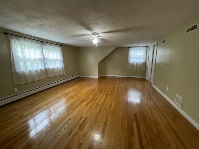 additional living space featuring baseboard heating, a ceiling fan, wood-type flooring, baseboards, and a textured ceiling