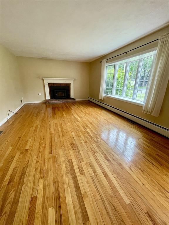 unfurnished living room with wood finished floors, a baseboard heating unit, a brick fireplace, and baseboards