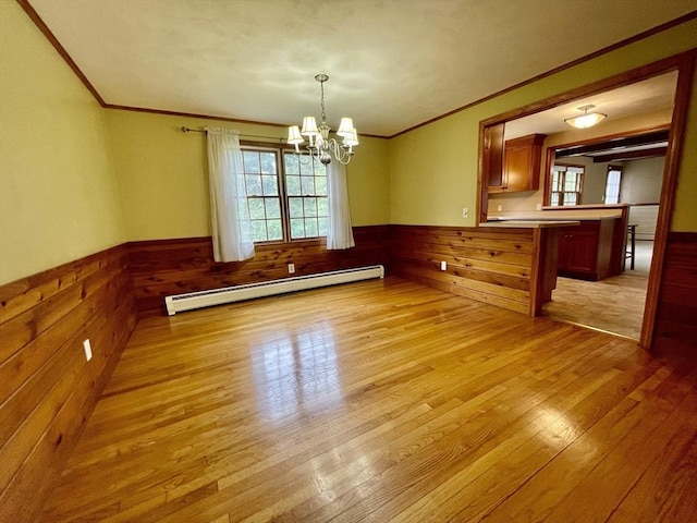 unfurnished dining area featuring baseboard heating, ornamental molding, wainscoting, light wood finished floors, and a chandelier