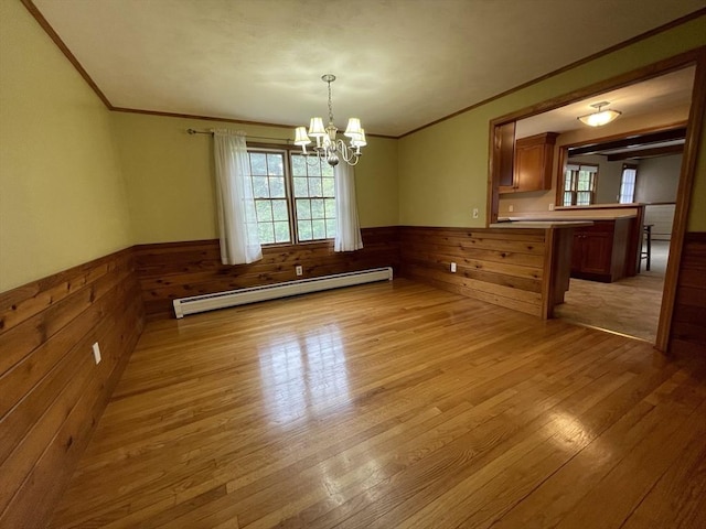 unfurnished dining area with a baseboard heating unit, crown molding, wainscoting, light wood-style floors, and a chandelier