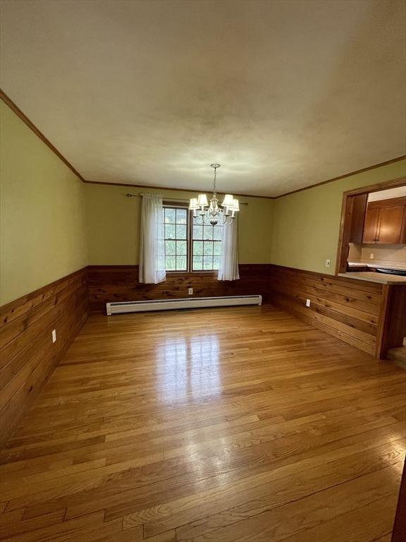 unfurnished dining area with wainscoting, a baseboard radiator, light wood-style floors, wooden walls, and a chandelier