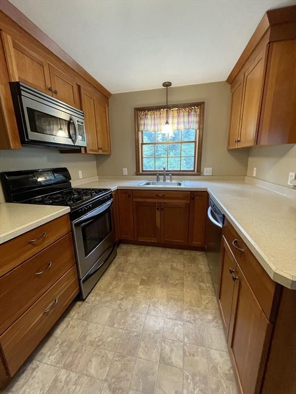 kitchen with appliances with stainless steel finishes, a sink, brown cabinets, light countertops, and hanging light fixtures