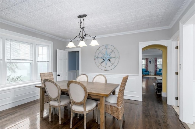 dining area featuring dark wood-type flooring, arched walkways, a chandelier, an ornate ceiling, and a wainscoted wall