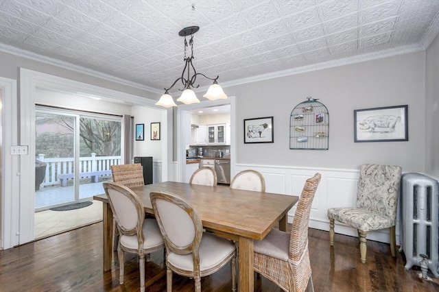 dining area featuring dark wood-style flooring, radiator heating unit, an ornate ceiling, ornamental molding, and a chandelier