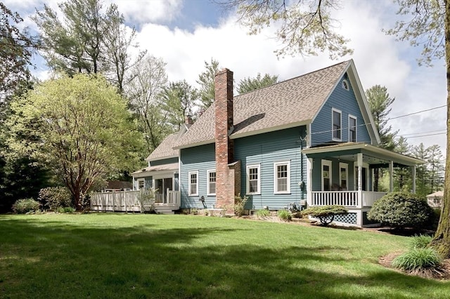 back of house with covered porch, a chimney, a yard, and a shingled roof