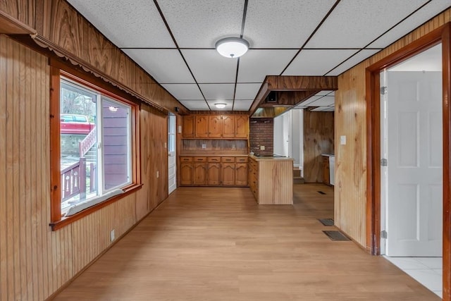 hallway with wooden walls, visible vents, a drop ceiling, and light wood-type flooring