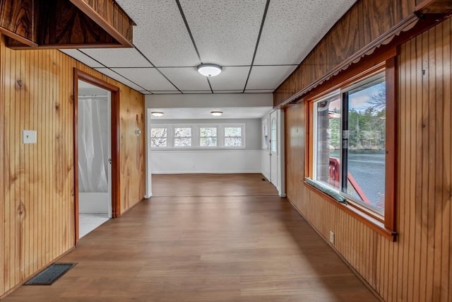 hall featuring wood walls, visible vents, a paneled ceiling, and light wood finished floors