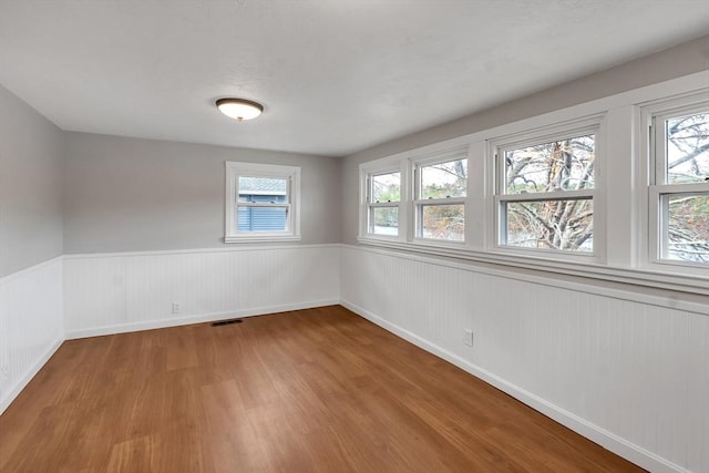spare room with a healthy amount of sunlight, wainscoting, wood finished floors, and visible vents