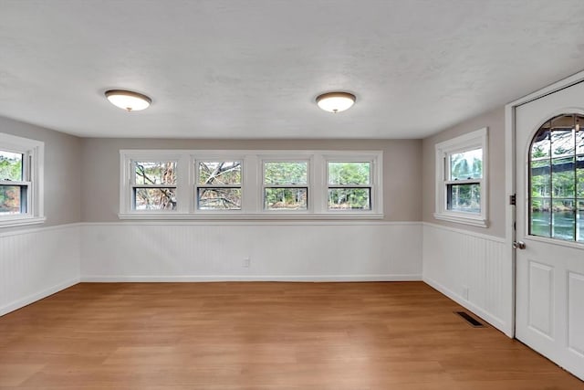 unfurnished room with a healthy amount of sunlight, a wainscoted wall, light wood-type flooring, and visible vents