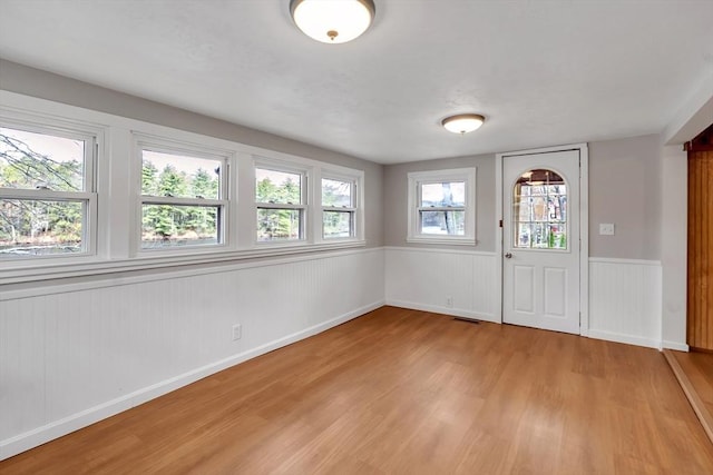 foyer with light wood-style floors, baseboards, wainscoting, and visible vents