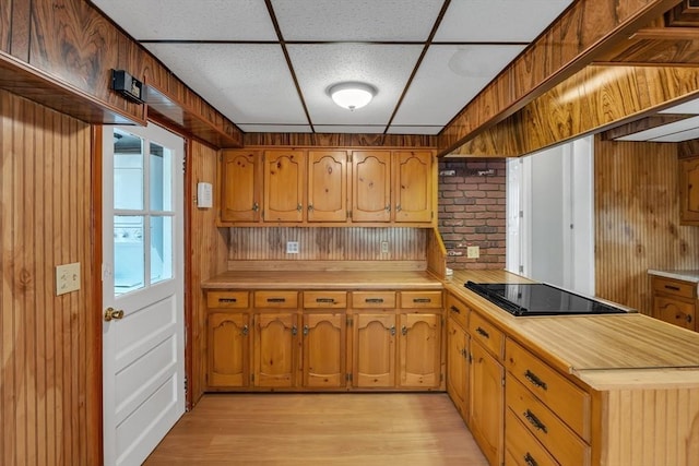 kitchen with brown cabinets, black electric cooktop, a paneled ceiling, a peninsula, and light wood-type flooring