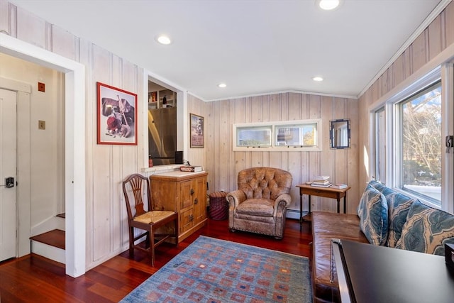 living area featuring baseboard heating, dark hardwood / wood-style floors, ornamental molding, and vaulted ceiling