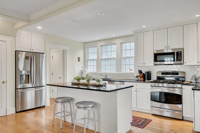 kitchen featuring appliances with stainless steel finishes, a breakfast bar, a kitchen island, light hardwood / wood-style flooring, and white cabinetry