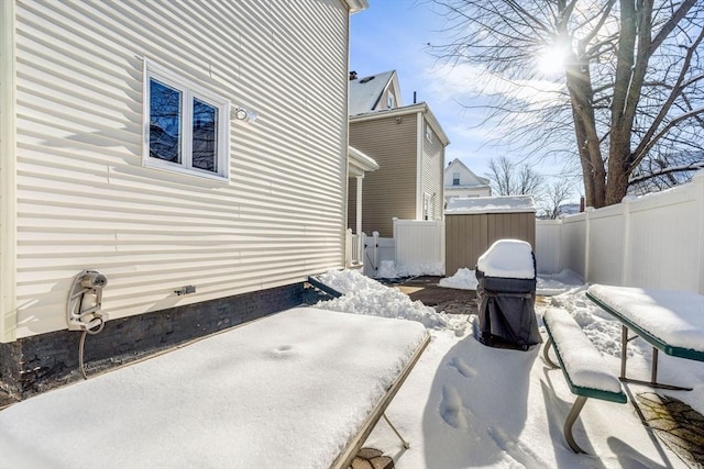 snow covered patio featuring a fenced backyard, an outdoor structure, and a storage unit