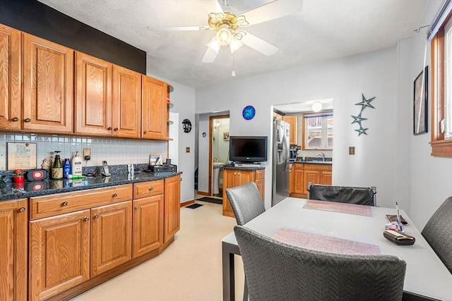 kitchen featuring decorative backsplash, brown cabinetry, a ceiling fan, a sink, and stainless steel fridge with ice dispenser