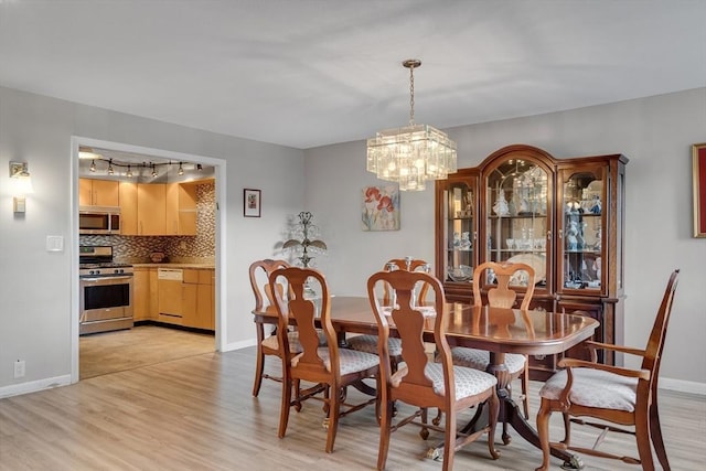 dining space with rail lighting, an inviting chandelier, and light hardwood / wood-style flooring