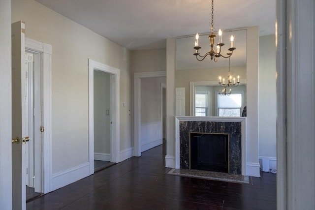 unfurnished living room featuring dark wood-type flooring, a high end fireplace, and a notable chandelier