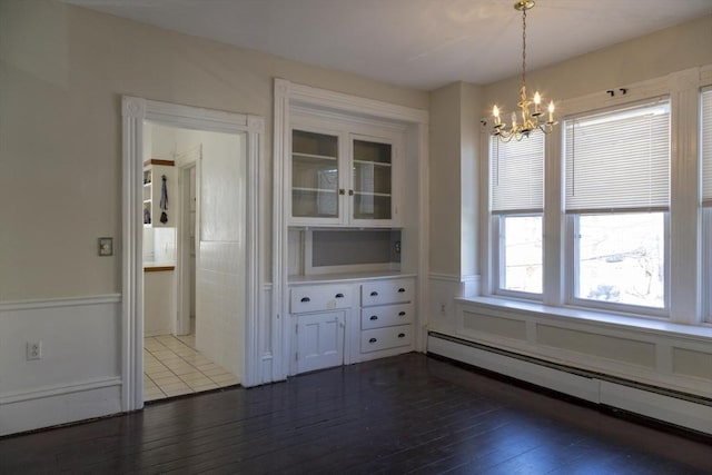 unfurnished dining area with dark wood-type flooring, a chandelier, and a baseboard radiator