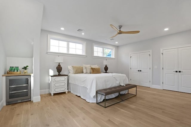 bedroom with ceiling fan, light hardwood / wood-style floors, wine cooler, and multiple closets