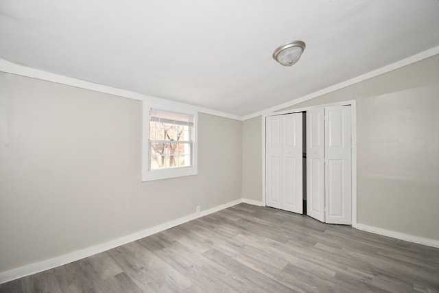 unfurnished bedroom featuring vaulted ceiling, crown molding, a closet, and light hardwood / wood-style flooring