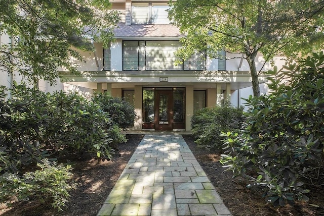 property entrance with stucco siding, roof with shingles, and french doors