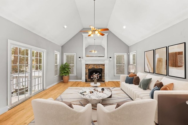 living room featuring ceiling fan, high vaulted ceiling, a stone fireplace, light wood-style flooring, and baseboards