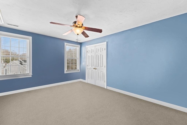 empty room with a wealth of natural light, carpet, visible vents, and baseboards