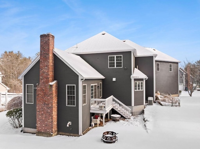 snow covered back of property featuring stairs, a chimney, central AC unit, and a deck