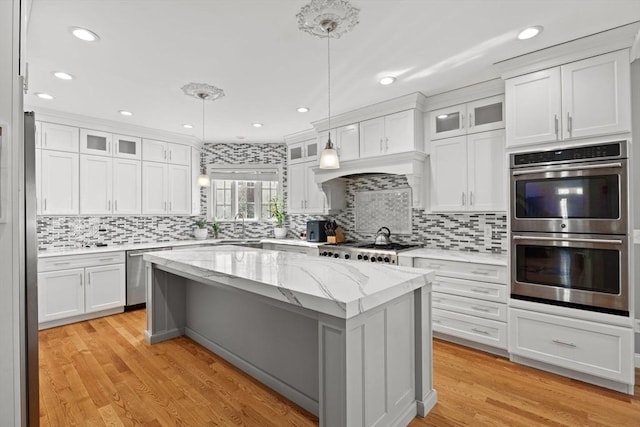 kitchen with hanging light fixtures, appliances with stainless steel finishes, glass insert cabinets, and white cabinets