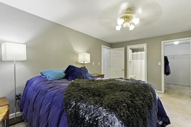 bedroom featuring baseboards, ceiling fan, light carpet, ensuite bath, and a walk in closet