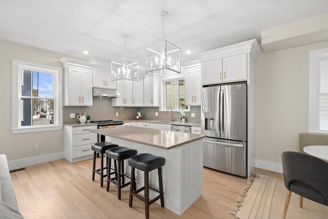 kitchen with under cabinet range hood, a kitchen island, white cabinetry, appliances with stainless steel finishes, and decorative light fixtures