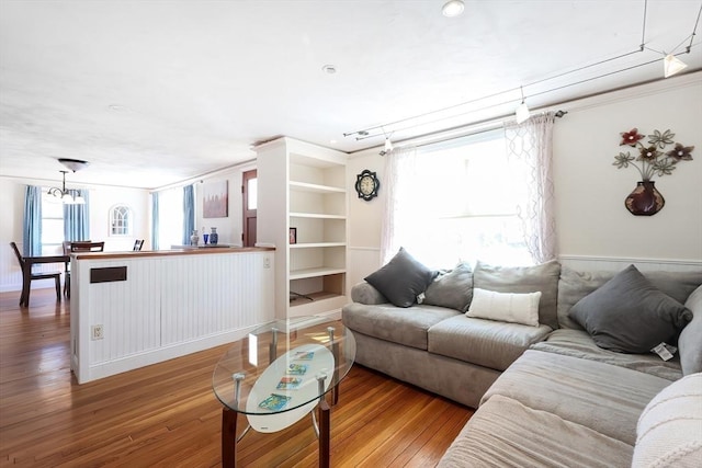living room featuring wood-type flooring, a chandelier, built in shelves, and ornamental molding