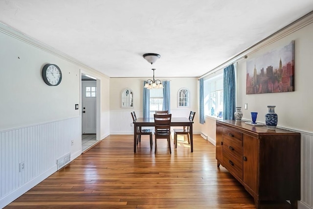 dining area featuring a chandelier, hardwood / wood-style floors, a wainscoted wall, and ornamental molding