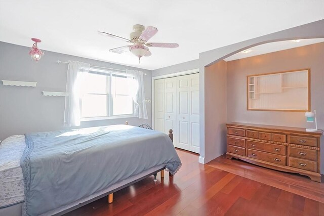 bedroom with arched walkways, wood finished floors, a closet, and a ceiling fan