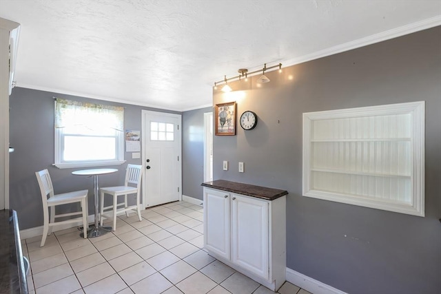 kitchen featuring baseboards, crown molding, light tile patterned flooring, dark countertops, and white cabinetry