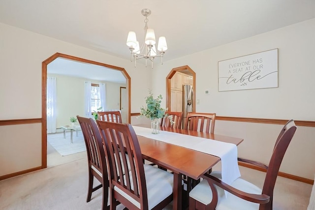 dining area with arched walkways, light colored carpet, baseboards, and an inviting chandelier