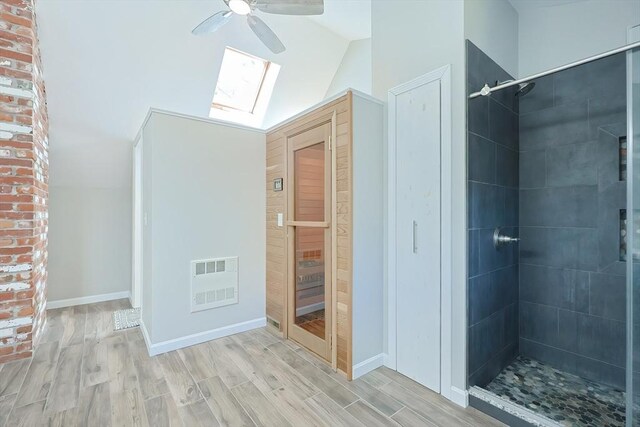 bathroom with visible vents, wood finished floors, vaulted ceiling with skylight, tiled shower, and ceiling fan