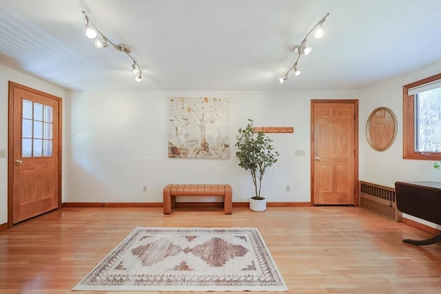 foyer featuring rail lighting, baseboards, radiator heating unit, and light wood-style floors