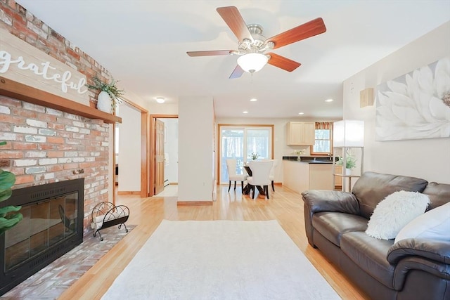 living area featuring a ceiling fan, baseboards, a fireplace, recessed lighting, and light wood-style floors