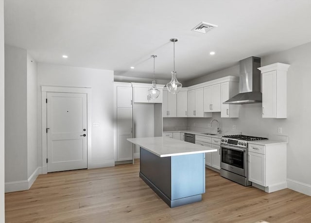 kitchen with stainless steel gas range oven, white cabinetry, a center island, hanging light fixtures, and wall chimney range hood