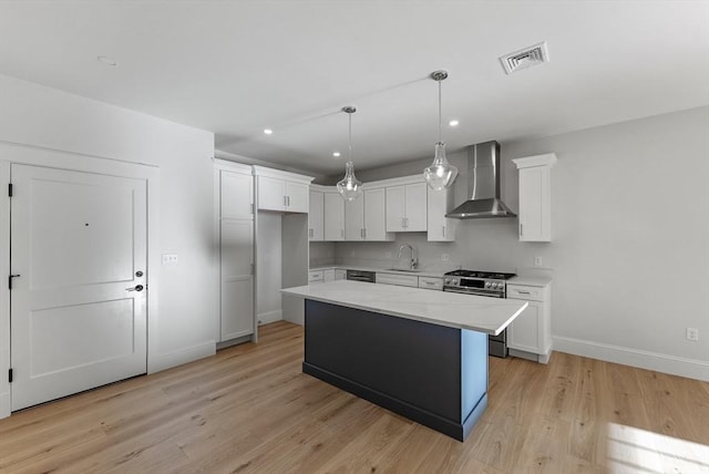 kitchen with white cabinets, stainless steel gas range, sink, and wall chimney exhaust hood