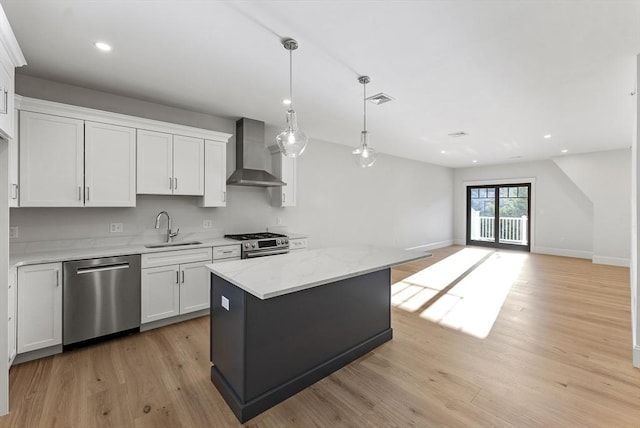 kitchen featuring wall chimney range hood, sink, appliances with stainless steel finishes, a center island, and white cabinets