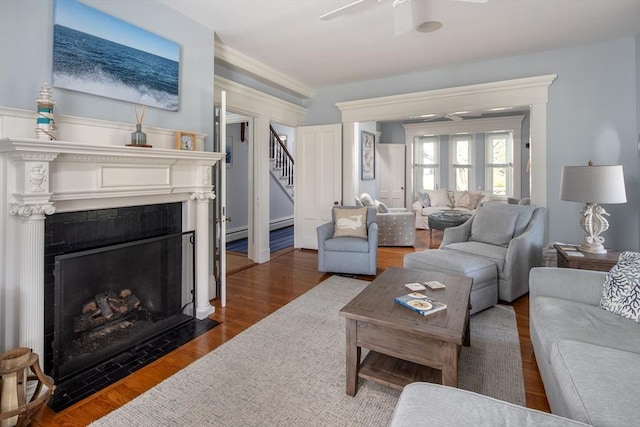 living area featuring stairway, ceiling fan, a fireplace with flush hearth, wood finished floors, and crown molding