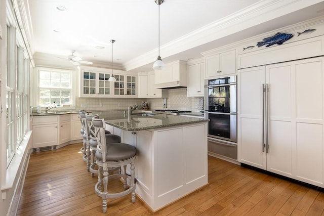 kitchen with stainless steel appliances, a warming drawer, a sink, tasteful backsplash, and white cabinets