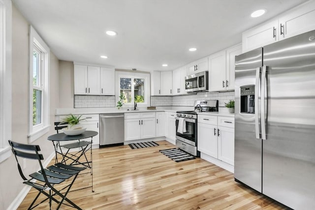 kitchen with stainless steel appliances, tasteful backsplash, light wood-type flooring, and white cabinetry