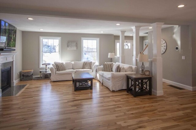 living room featuring a fireplace with flush hearth, visible vents, wood finished floors, baseboards, and decorative columns