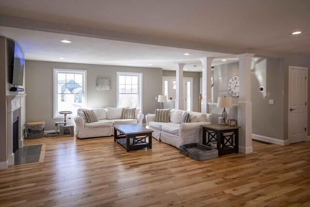 living room featuring baseboards, a fireplace with flush hearth, wood finished floors, ornate columns, and recessed lighting